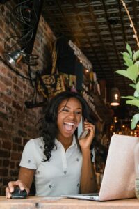 Excited small business owner laughing while talking on phone in a cozy bar setting.
